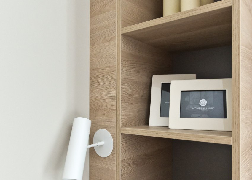 Ein Holzregal mit Kerzen, Bilderrahmen und einer wei&szlig;en Wandlampe. Die Deko ist minimalistisch und modern., &copy; Arthotel Ana / elaya
