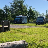 Wohnmobilstellplatz mit zwei Wohnmobilen, Holztisch und Bänken unter einem blühenden Baum. Im Hintergrund sind kleine Holzhütten zu sehen., © Bio Weingut Zimmer Wohnmobilstellplatz mit zwei Wohnmobilen, Holztisch und Bänken unter einem blühenden Baum. Im Hintergrund sind kleine Holzhütten zu sehen., © Bio Weingut Zimmer