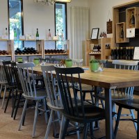 Wine bar with wooden table and chairs, surrounded by wine racks and decorations. Bright, inviting atmosphere with wine bottles and plants., © Weinfactum Bad Cannstatt Wine bar with wooden table and chairs, surrounded by wine racks and decorations. Bright, inviting atmosphere with wine bottles and plants., © Weinfactum Bad Cannstatt