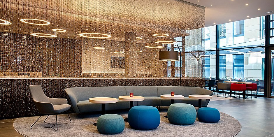 Moderne Lobby mit grauem Sofa, blauen Hockern und runden Tischen vor einer glitzernden Wand., © Holiday Inn Express Waiblingen Moderne Lobby mit grauem Sofa, blauen Hockern und runden Tischen vor einer glitzernden Wand., © Holiday Inn Express Waiblingen