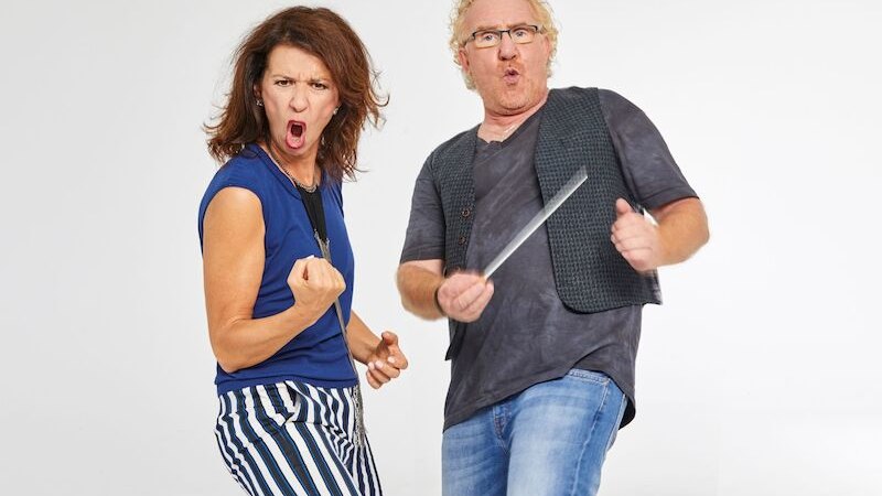 Zwei Personen posieren energisch vor einem weißen Hintergrund. Eine Frau in gestreifter Hose und ein Mann mit Brille und Weste., © Theaterhaus Stuttgart e.V.