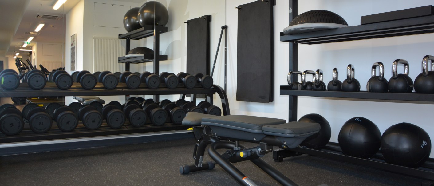 Ein modernes Fitnessstudio mit Hanteln, Kettlebells und Gymnastikbällen. Eine Trainingsbank steht im Vordergrund, Spiegel an der Wand., © Aloft Stuttgart Ein modernes Fitnessstudio mit Hanteln, Kettlebells und Gymnastikbällen. Eine Trainingsbank steht im Vordergrund, Spiegel an der Wand., © Aloft Stuttgart