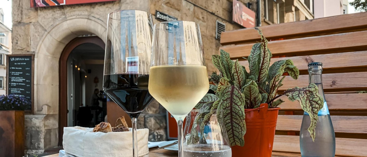 Zwei Weingläser und eine Wasserflasche auf einem Tisch vor dem Restaurant 'Speisekammer West'. Im Hintergrund ein steinerner Eingang., © Speisekammer West, Stuttgart