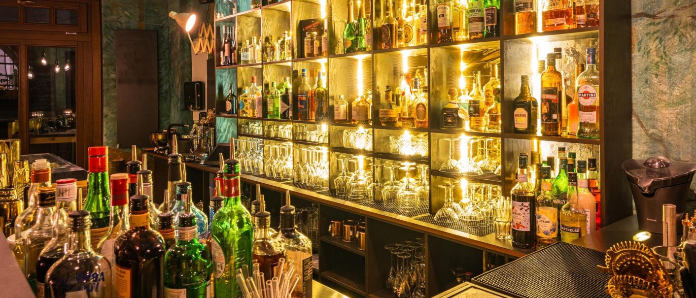 Eine stilvolle Bar mit beleuchteten Regalen, gefüllt mit verschiedenen Flaschen und Gläsern. Die Atmosphäre ist warm und einladend., © Holzmaler, Stuttgart