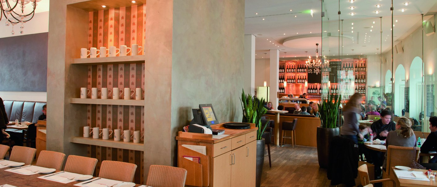 Stilvolles Restaurant mit Holzmöbeln, Regalen mit Tassen und einer Bar im Hintergrund. Menschen sitzen an Tischen, moderne Beleuchtung und Pflanzen dekorieren den Raum., © aspectus photographie, Stuttgart Stilvolles Restaurant mit Holzmöbeln, Regalen mit Tassen und einer Bar im Hintergrund. Menschen sitzen an Tischen, moderne Beleuchtung und Pflanzen dekorieren den Raum., © aspectus photographie, Stuttgart