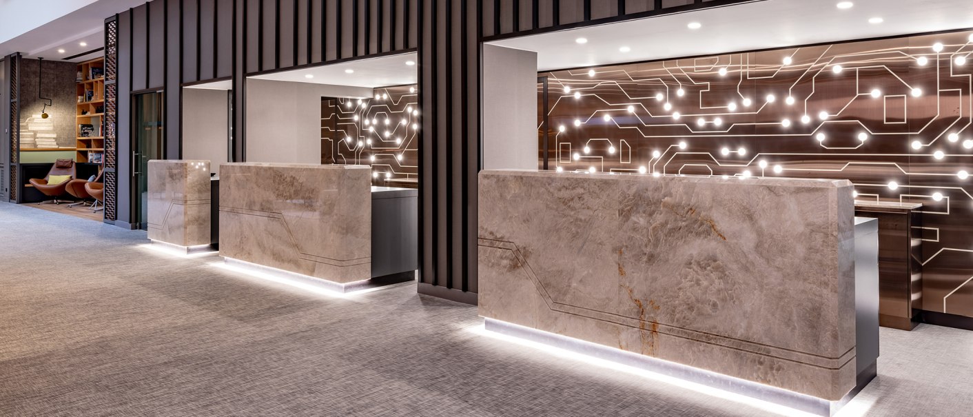 Modern reception with marble counters and illuminated wall. Cozy sitting area with armchairs and bookshelf on the left., © Stuttgart Marriott Hotel Sindelfingen Modern reception with marble counters and illuminated wall. Cozy sitting area with armchairs and bookshelf on the left., © Stuttgart Marriott Hotel Sindelfingen