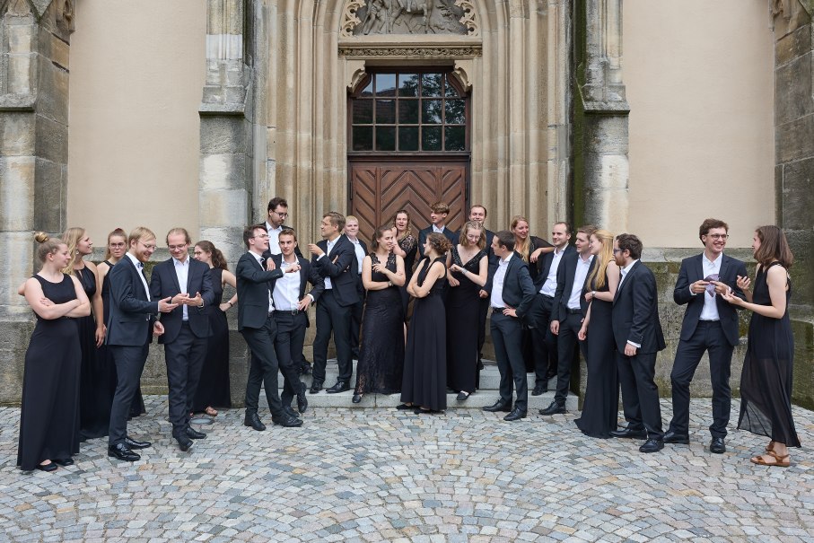Eine Gruppe von Menschen in eleganter Abendkleidung steht vor einem alten Geb&auml;ude mit verzierten T&uuml;ren und Steinmauern., &copy; collegium vocale Stuttgart