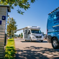 Wohnmobilstellplatz mit einem weißen Wohnmobil und einem blauen Van. Im Vordergrund eine Stromsäule, im Hintergrund Bäume und blauer Himmel., © Stuttgart-Marketing GmbH, Thomas Niedermüller