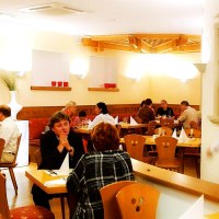 Gem&uuml;tliches Restaurant mit Holzm&ouml;beln, mehreren G&auml;sten an Tischen und einem Kellner in Bewegung. Warme Beleuchtung und dekorative Elemente an den W&auml;nden., &copy; SMG