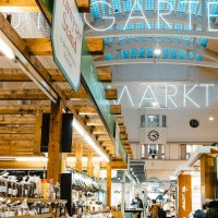 Interior view of the Stuttgart market hall with wooden stalls, illuminated signage and various delicatessen stalls., © by Canto