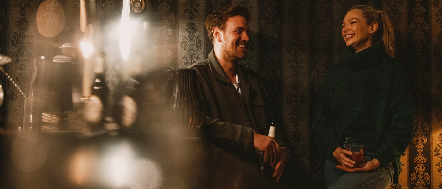 Zwei Personen lachen in einer gemütlichen Bar mit gedämpfter Beleuchtung und dekorativer Tapete im Hintergrund., © Stuttgart Marketing GmbH, Fotograf Alwin Maigler