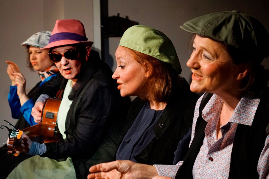 Vier Personen auf einer Bühne, eine spielt Gitarre. Sie tragen bunte Hüte und sind in eine lebhafte Unterhaltung vertieft., © Katja Ritter