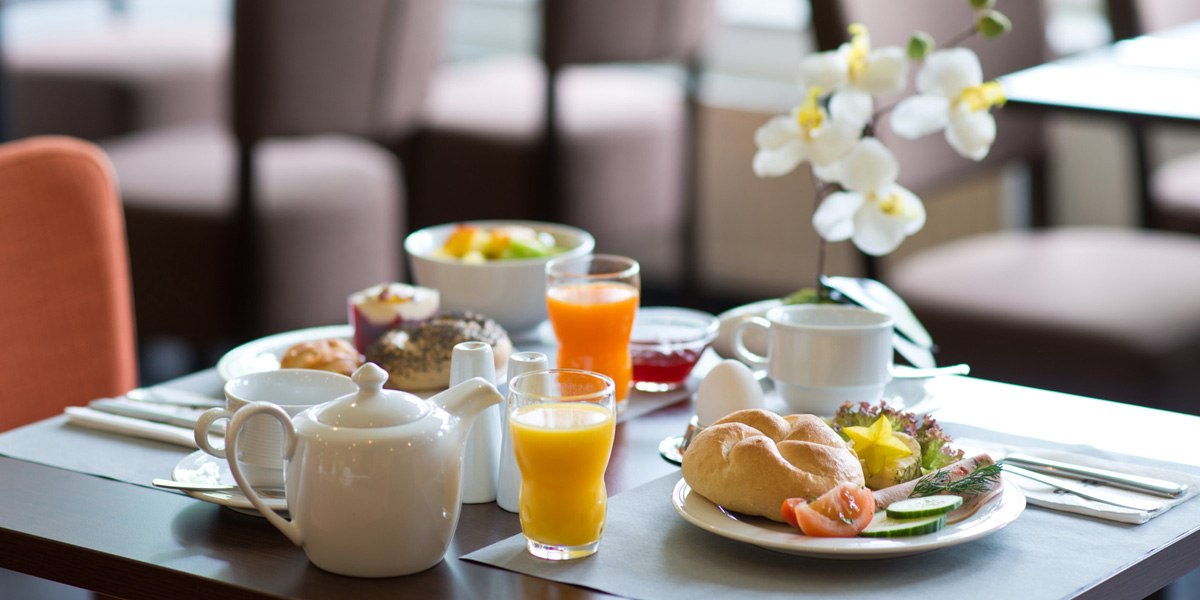 A breakfast table set with rolls, orange juice, tea, fruit, an egg, and an orchid as a decoration., &copy; ACHAT Hotels Deutschland