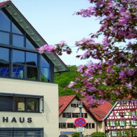 The modern town hall of Bad Ueberkingen with large windows and red roof. Flowering trees in the foreground, traditional half-timbered houses in the background., © © Stuttgart-Marketing GmbH