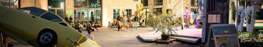 Evening event at the Kunstverein Wagenhalle with an art installation of a yellow car and people sitting in the square watching a performance., © Atelier Oradoro Evening event at the Kunstverein Wagenhalle with an art installation of a yellow car and people sitting in the square watching a performance., © Atelier Oradoro