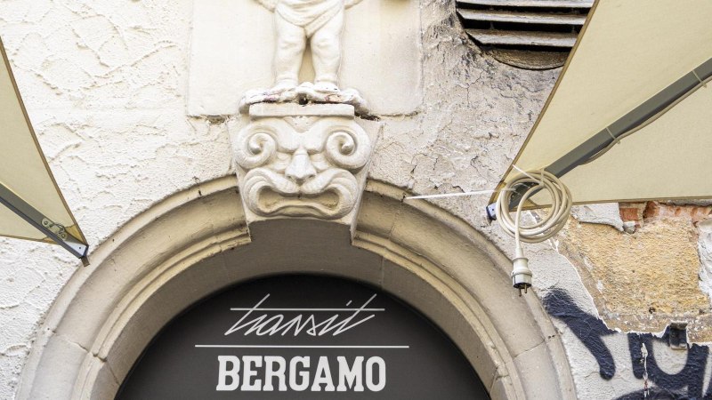 Steinfigur über einem Torbogen mit der Aufschrift 'transit BERGAMO'. Graffiti und verwitterte Wand im Hintergrund., © SMG, Sarah Schmid