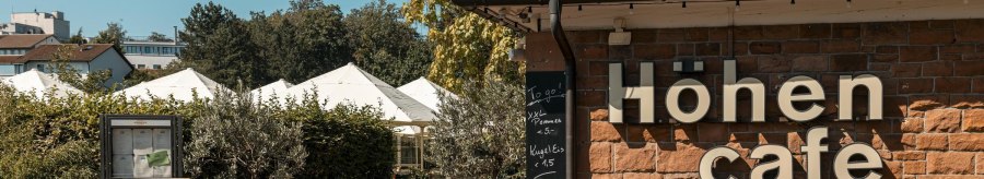 Das Höhen Café mit Schildern und Pflanzen im Außenbereich bei sonnigem Wetter., © SMG Stuttgart Marketing GmbH - Sarah Schmid Das Höhen Café mit Schildern und Pflanzen im Außenbereich bei sonnigem Wetter., © SMG Stuttgart Marketing GmbH - Sarah Schmid