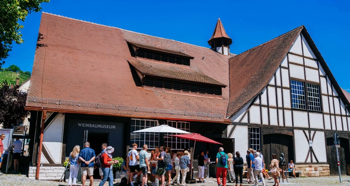 Besucher stehen vor dem Weinbaumuseum Uhlbach. Das Fachwerkgebäude hat ein rotes Ziegeldach. Der Himmel ist klar und blau., © Stuttgart-Marketing GmbH, Thomas Niedermüller Besucher stehen vor dem Weinbaumuseum Uhlbach. Das Fachwerkgebäude hat ein rotes Ziegeldach. Der Himmel ist klar und blau., © Stuttgart-Marketing GmbH, Thomas Niedermüller
