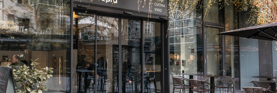 Eingang eines Caf&eacute;s mit Glasfront und Au&szlig;enbestuhlung. Pflanzen h&auml;ngen von oben herab. Menschen sitzen drinnen. Schild mit 'sotto sopra' sichtbar., &copy; SMG, Sarah Schmid