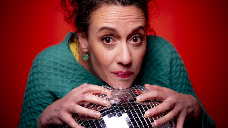 Frau in grünem Pullover hält eine Discokugel vor einem roten Hintergrund und schaut in die Kamera., © Rosenau Kultur e.V. Frau in grünem Pullover hält eine Discokugel vor einem roten Hintergrund und schaut in die Kamera., © Rosenau Kultur e.V.