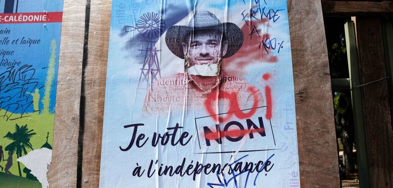 Ein beschädigtes Wahlplakat in Neukaledonien mit der Aufschrift 'Je vote NON à l'indépendance', das mit Graffiti und Rissen versehen ist., © Theo Rouby / Hans Lucas