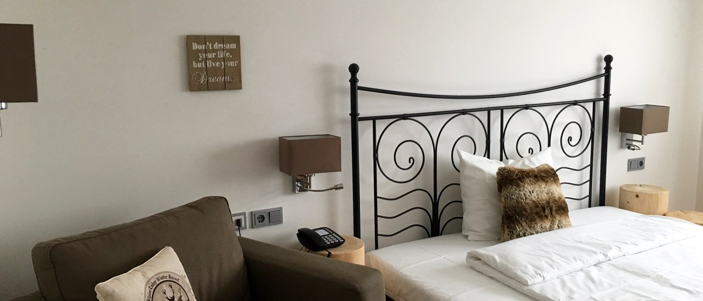 Modernes Schlafzimmer mit Metallbett, braunem Sessel und dekorativen Kissen. An der Wand hängen motivierende Sprüche., © TOMAS