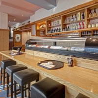 A Japanese restaurant with a sushi counter, bar stools and shelves full of sake bottles. Wooden elements dominate the interior., &copy; Martin Frey