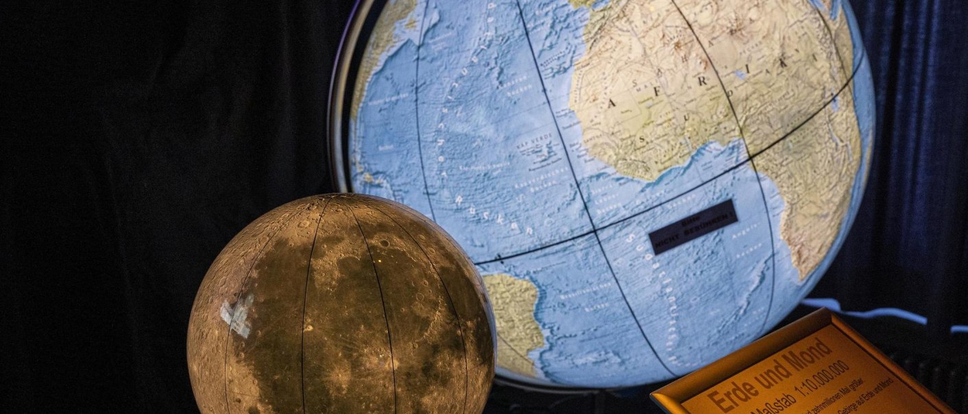 Ein Globus der Erde und ein Mondmodell im Carl-Zeiss Planetarium Stuttgart, mit einer Informationstafel über Maßstab und Entfernung., © Stuttgart-Marketing GmbH, Sarah Schmid
