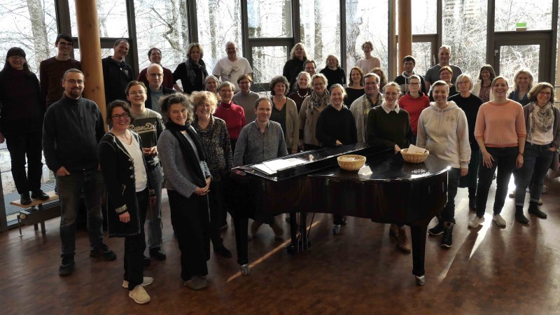 Eine Gruppe von Menschen steht um einen Flügel in einem Raum mit großen Fenstern. Sie lächeln und posieren für ein Foto., © Uni Hohenheim / Uni-Chor