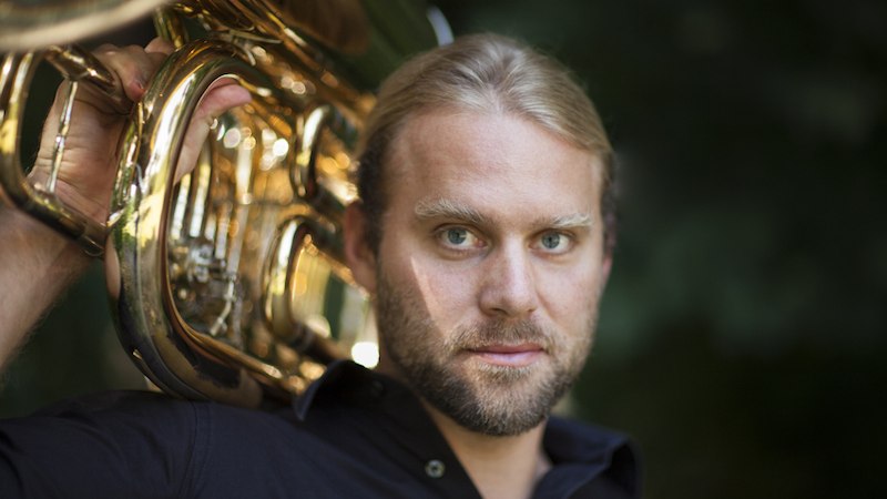 Ein Mann mit blonden Haaren und Bart h&auml;lt eine gl&auml;nzende Tuba auf der Schulter. Er tr&auml;gt ein schwarzes Hemd und blickt direkt in die Kamera., &copy; Rosenau Kultur e.V.