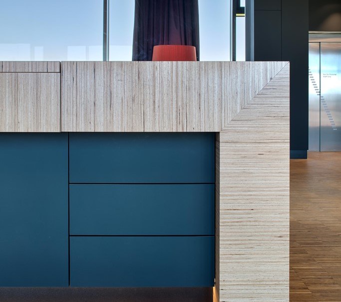 Modern reception desk with blue drawers and wooden paneling, illuminated from below. A red chair and large windows in the background., &copy; Hotel am Remspark