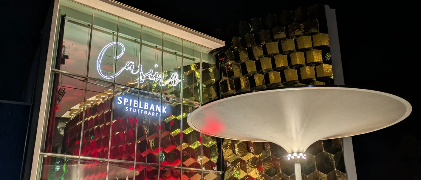 Die Spielbank Stuttgart bei Nacht: beleuchtete Glasfassade, goldene Kubusstruktur und markantes wei&szlig;es Schirmdach., &copy; SMG