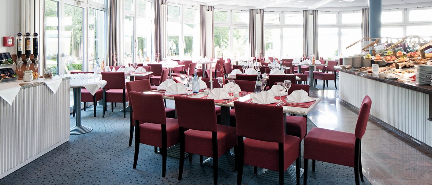 Elegantes Buffet-Restaurant mit roten St&uuml;hlen, gedeckten Tischen und gro&szlig;en Fenstern. Ein Buffet mit Speisen ist rechts zu sehen., &copy; Seminaris Hotel Bad Boll