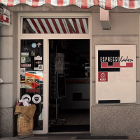 Espressoladen in Stuttgart-S&uuml;d mit rot-wei&szlig; gestreifter Markise, Schaufenster und Eingangst&uuml;r. Aufkleber und Kaffees&auml;cke sind sichtbar., &copy; Espressoladen, Stuttgart