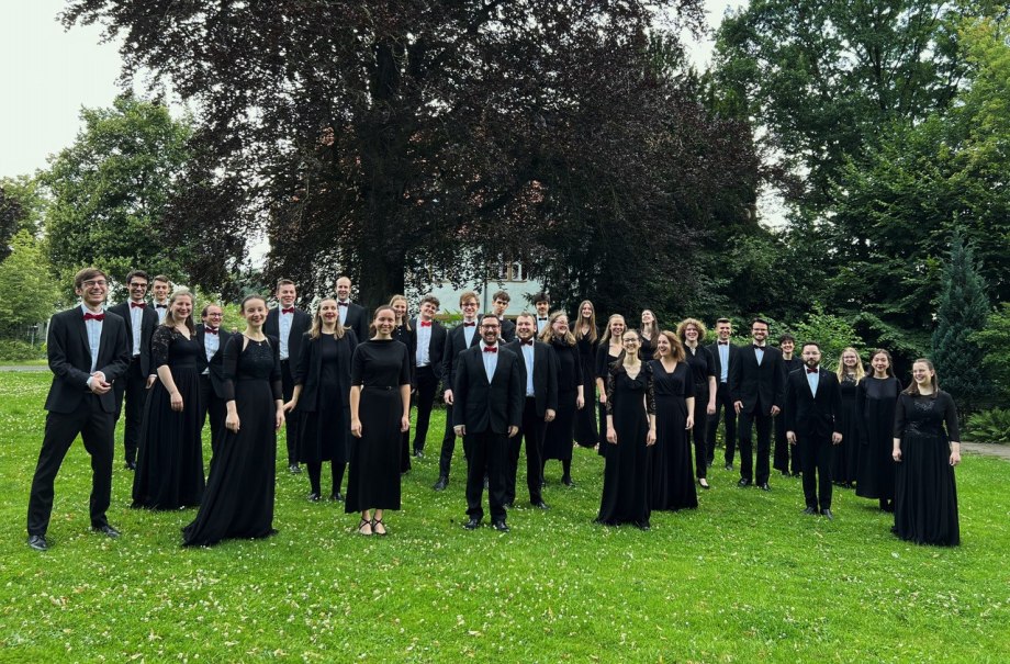 Der Kammerchor der Hochschule f&uuml;r Musik Detmold posiert in eleganter Kleidung auf einer gr&uuml;nen Wiese vor einem gro&szlig;en Baum., &copy; Kammerchor der Hochschule f&uuml;r Musik Detmold