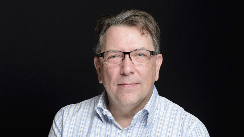 Ein Mann mit Brille und gestreiftem Hemd lächelt leicht in die Kamera. Der Hintergrund ist schwarz, was den Fokus auf das Gesicht lenkt., © Foto: Gerrit Mumme Ein Mann mit Brille und gestreiftem Hemd lächelt leicht in die Kamera. Der Hintergrund ist schwarz, was den Fokus auf das Gesicht lenkt., © Foto: Gerrit Mumme