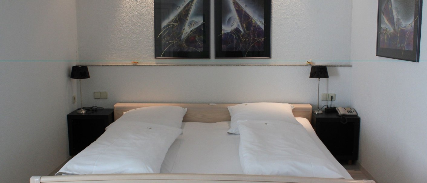 A hotel room with a double bed, two nightstands with lamps, and abstract paintings on the wall., &copy; Hotel Spahr