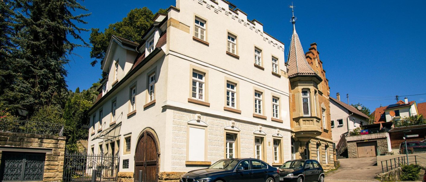 A historic building in Vaihingen an der Enz with a distinctive turret and parked cars in front of it, surrounded by trees and blue sky., © Stuttgart-Marketing GmbH, Sarah Schmid A historic building in Vaihingen an der Enz with a distinctive turret and parked cars in front of it, surrounded by trees and blue sky., © Stuttgart-Marketing GmbH, Sarah Schmid