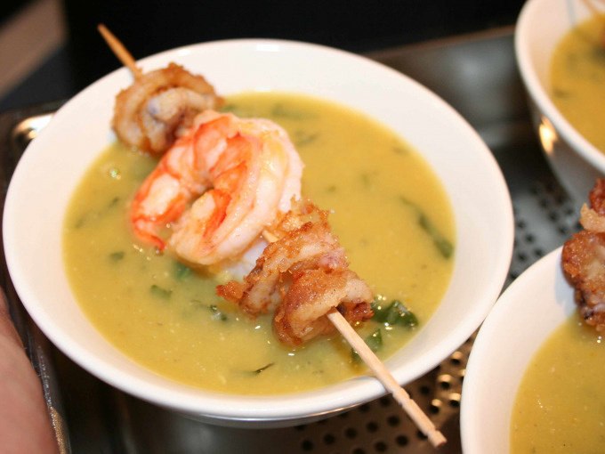 A bowl of yellow soup garnished with a skewer of prawns and fried meat., © Kultweine-Kochwelten-Kunstücke - Kochschule Sonja Lenz A bowl of yellow soup garnished with a skewer of prawns and fried meat., © Kultweine-Kochwelten-Kunstücke - Kochschule Sonja Lenz