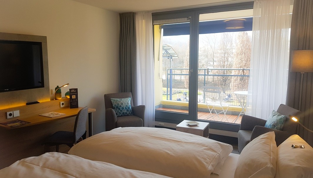 Modernes Doppelzimmer mit großem Bett, Schreibtisch, Fernseher und Balkon mit Ausblick auf Bäume., © ©hotel-graf-eberhard.de