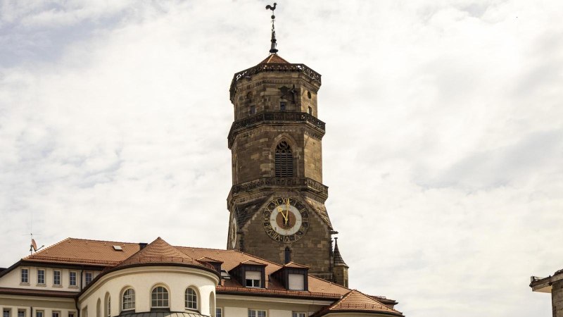 Tower of the collegiate church in Stuttgart with clock and weathercock, surrounded by buildings under a cloudy sky., &copy; SMG Stuttgart Marketing GmbH - Sarah Schmid