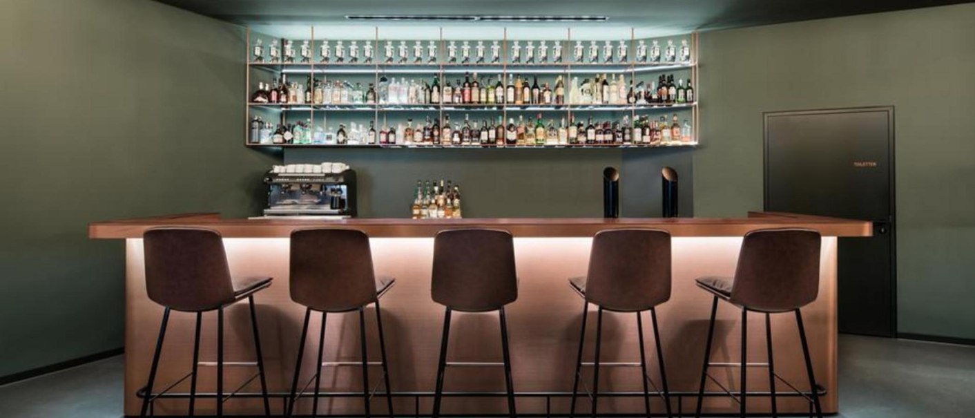 Moderne Bar mit hohen Stühlen, beleuchtetem Tresen und Flaschenregal im Hintergrund. Dezente Beleuchtung und schlichte Einrichtung., © Eduards Bar, Stuttgart