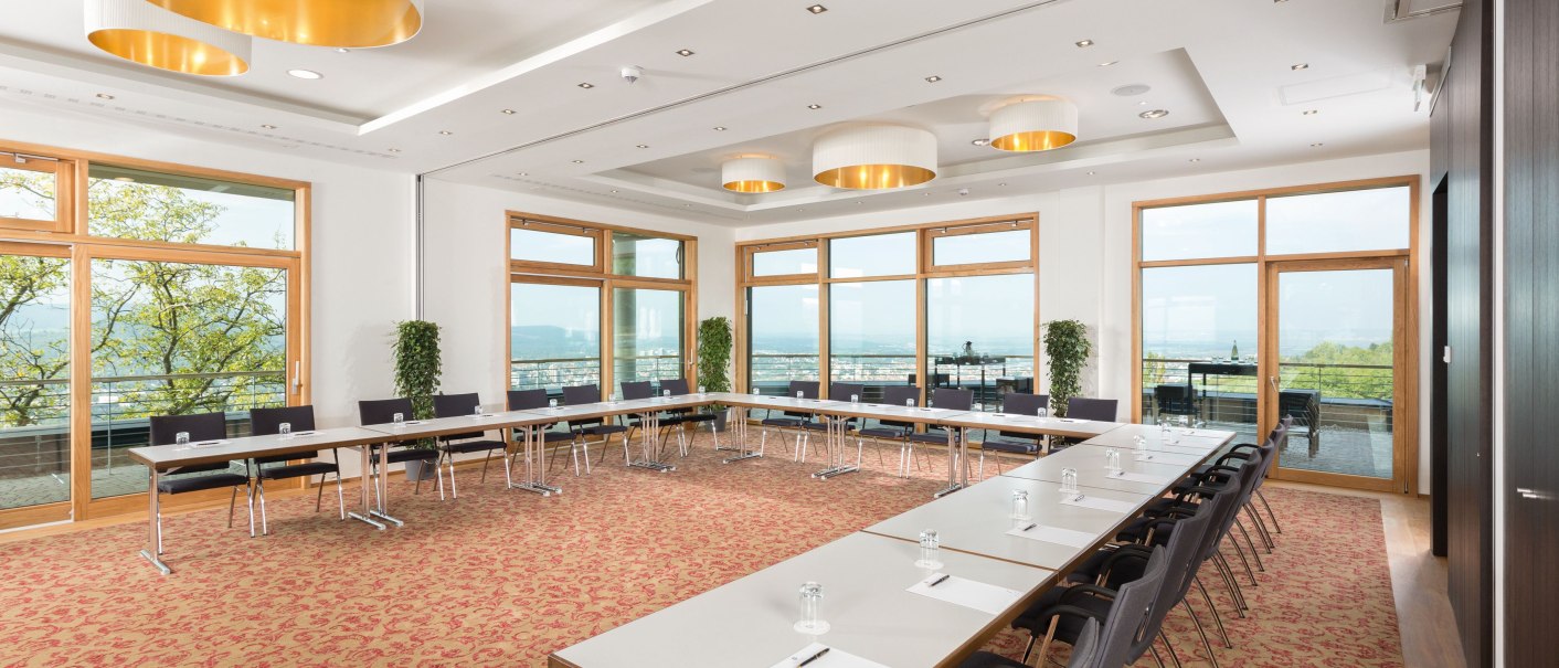 Tagungsraum mit U-förmiger Tischanordnung, großen Fenstern und eleganten Deckenleuchten. Heller Teppichboden und Blick ins Freie., © Achalm. Hotel GmbH & Co. KG Tagungsraum mit U-förmiger Tischanordnung, großen Fenstern und eleganten Deckenleuchten. Heller Teppichboden und Blick ins Freie., © Achalm. Hotel GmbH & Co. KG