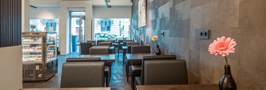 Modern café with dark tables and chairs, vases of flowers on the tables and a cake display case in the background., © Café LIST, Stuttgart