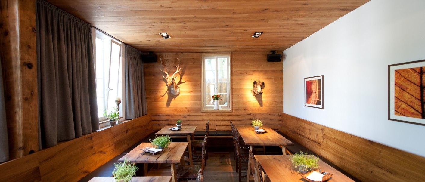Ein gemütliches Restaurant mit Holztischen, Pflanzen auf den Tischen und dekorativen Elementen an den Wänden. Holzwände und -decke schaffen eine warme Atmosphäre., © Ruthenberg&Schlatter GbR Ein gemütliches Restaurant mit Holztischen, Pflanzen auf den Tischen und dekorativen Elementen an den Wänden. Holzwände und -decke schaffen eine warme Atmosphäre., © Ruthenberg&Schlatter GbR