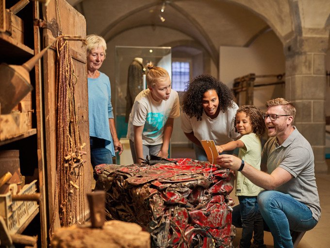 Eine Gruppe von fünf Personen, darunter Kinder und Erwachsene, betrachtet interessiert eine Ausstellung im Museum der Alltagskultur., © Landesmuseum Württemberg Eine Gruppe von fünf Personen, darunter Kinder und Erwachsene, betrachtet interessiert eine Ausstellung im Museum der Alltagskultur., © Landesmuseum Württemberg