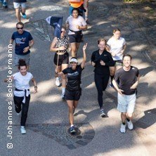 Eine Gruppe von Menschen joggt fr&ouml;hlich auf einem sonnigen Weg. Sie tragen sportliche Kleidung und wirken motiviert., &copy; links im Bild