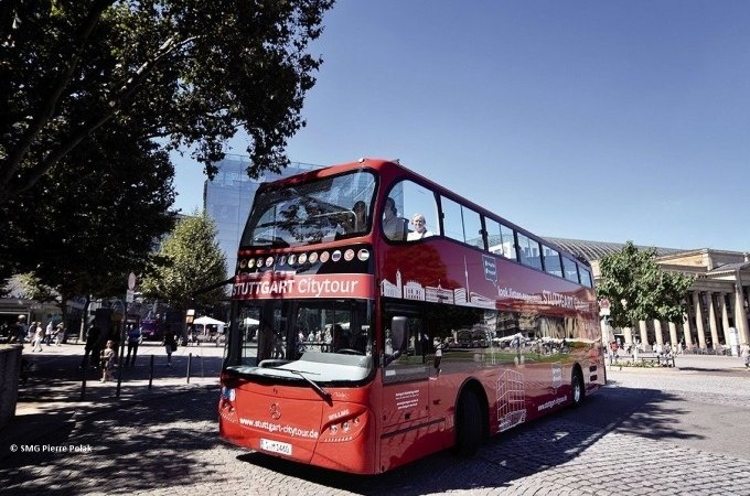 Roter Doppeldeckerbus der Stuttgart Citytour auf einem gepflasterten Platz, umgeben von Bäumen und Gebäuden., © SMG, Pierre Polak