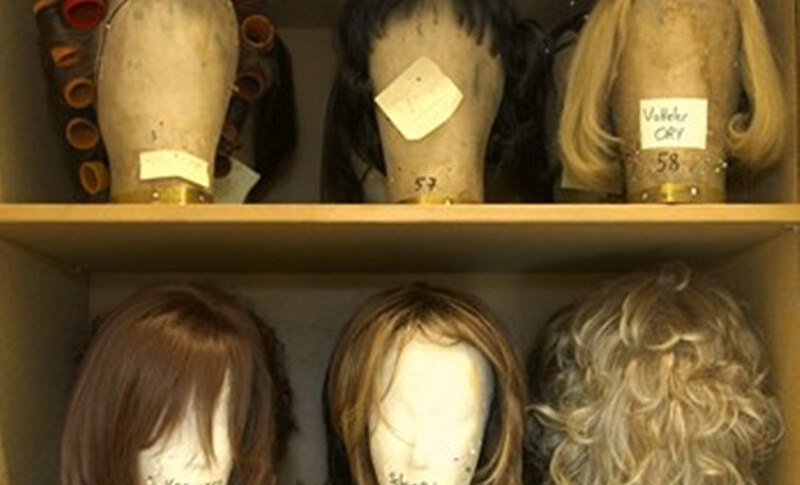 Regal mit sechs Per&uuml;cken auf Styropork&ouml;pfen, einige mit Lockenwicklern. Beschriftungen auf den K&ouml;pfen sind sichtbar., &copy; W&uuml;rttembergische Staatstheater Stuttgart