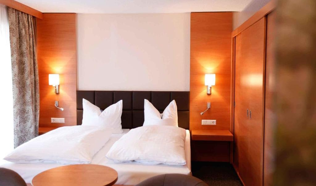 Cozy double room with wooden furniture, large bed, two bedside lamps and a small table with two armchairs., © Nödinger Gastro GmbH
